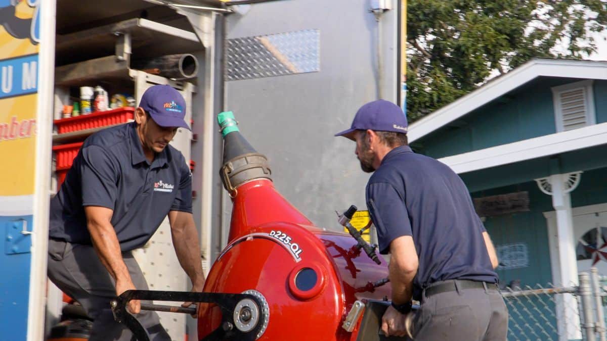 Two All Aloha Plumbing technicians handling a hydro jetting machine at a job site